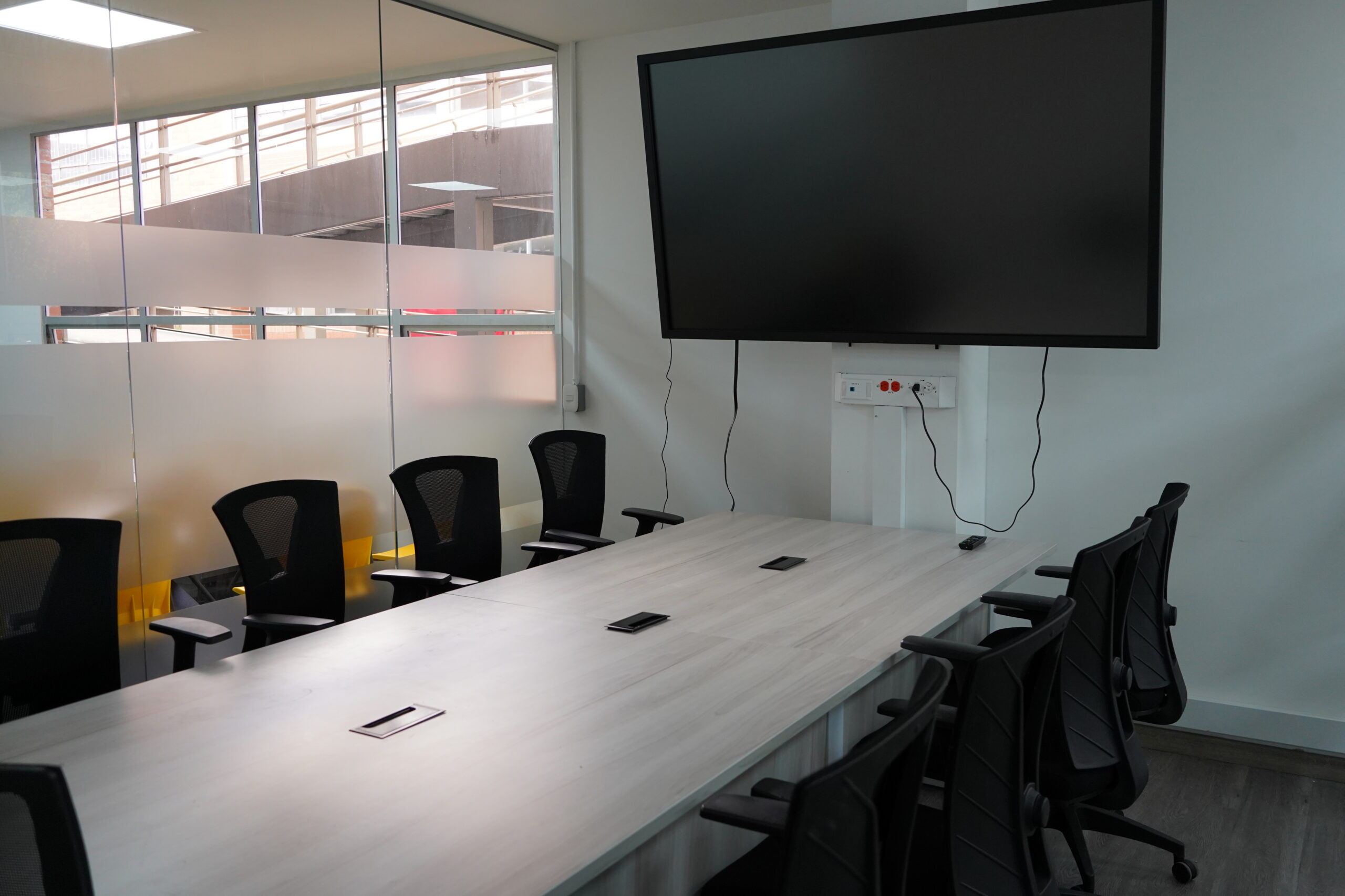 Glass-enclosed boardroom with long table, ergonomic chairs and screen