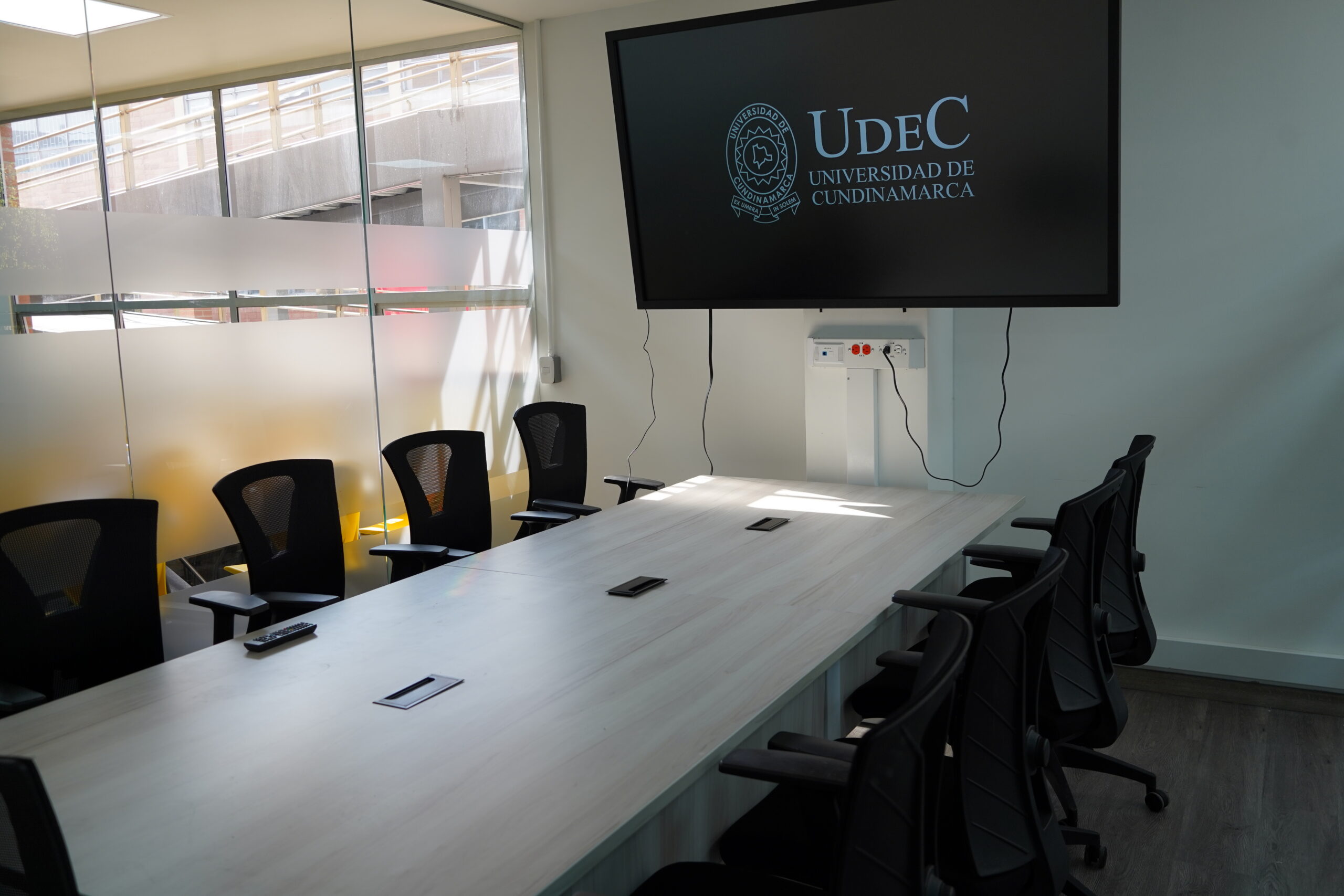 Sala de juntas con una pantalla que muestra el escudo de la Universidad de Cundinamarca