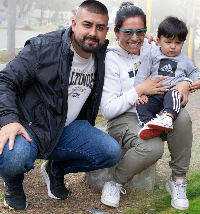Una pareja y su hijo pequeño, sentados y sonriendo, en una zona verde de la Universidad de Cundinamarca