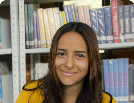 Estudiante de la sede Facatativá sonriendo frente a una estantería de libros